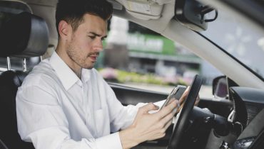 Motorista de Uber dentro do carro com celular na mão olhando aplicativo para descobrir o preço das corridas antes de aceitar